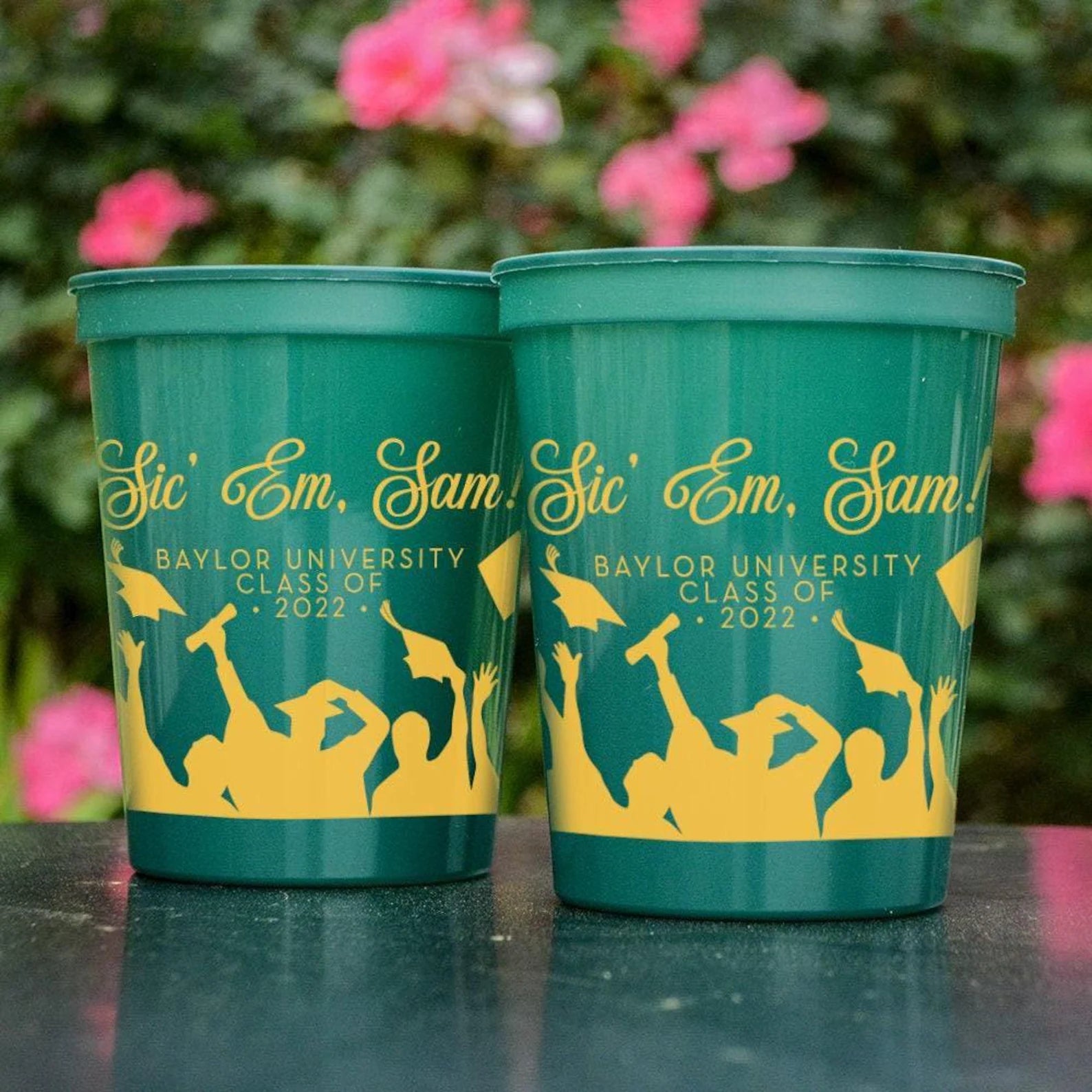 Two green plastic cups with yellow text and graphics, likely representing a graduation or celebration event at Baylor University.