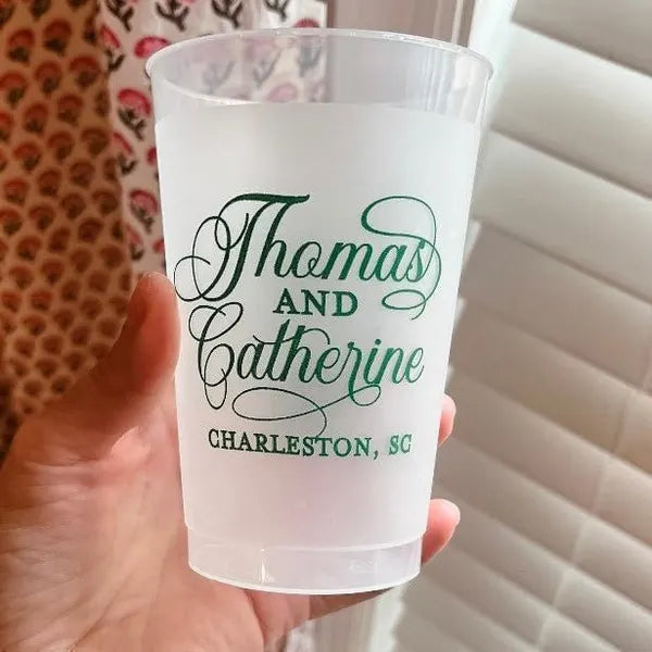 A person's hand holding a clear plastic cup with the text "Thomas and Catherine Charleston SC" printed on it.