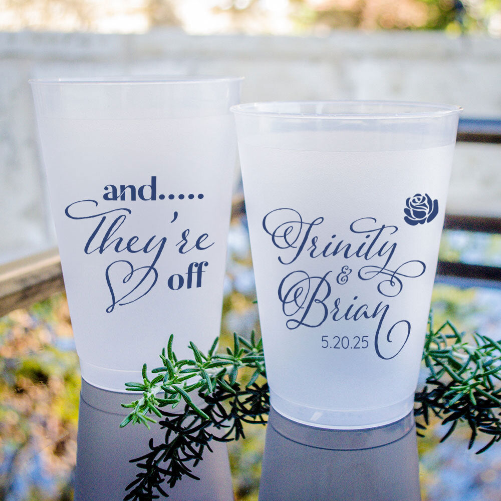 Two white plastic cups with text printed on them, placed on a table with greenery.