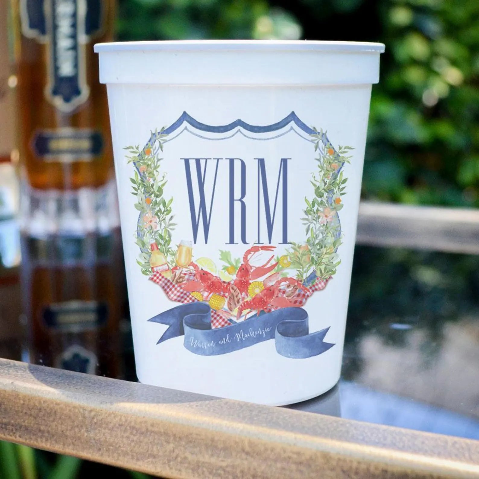 A white plastic cup with a decorative design featuring a lobster and other seafood items, along with the letters "WRM" and the text "Waters and Mussels".